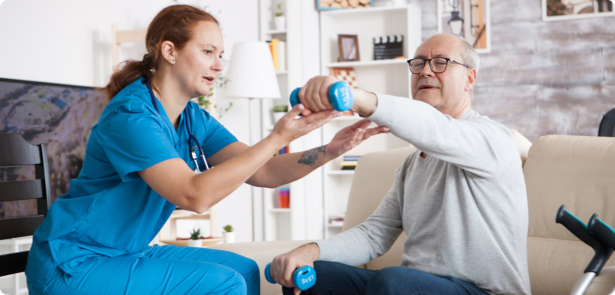 Physical therapist helping an elderly man with dumbbell exercises.