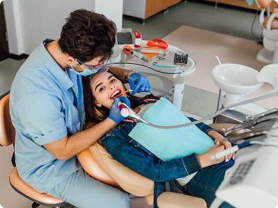 A dentist or dental assistant in blue scrubs using a digital intraoral scanner on a smiling female patient in a modern dental office.