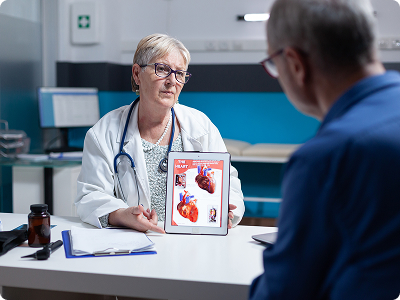 A cardiologist in a white coat showing a digital tablet with a detailed heart diagram to a patient during a consultation.