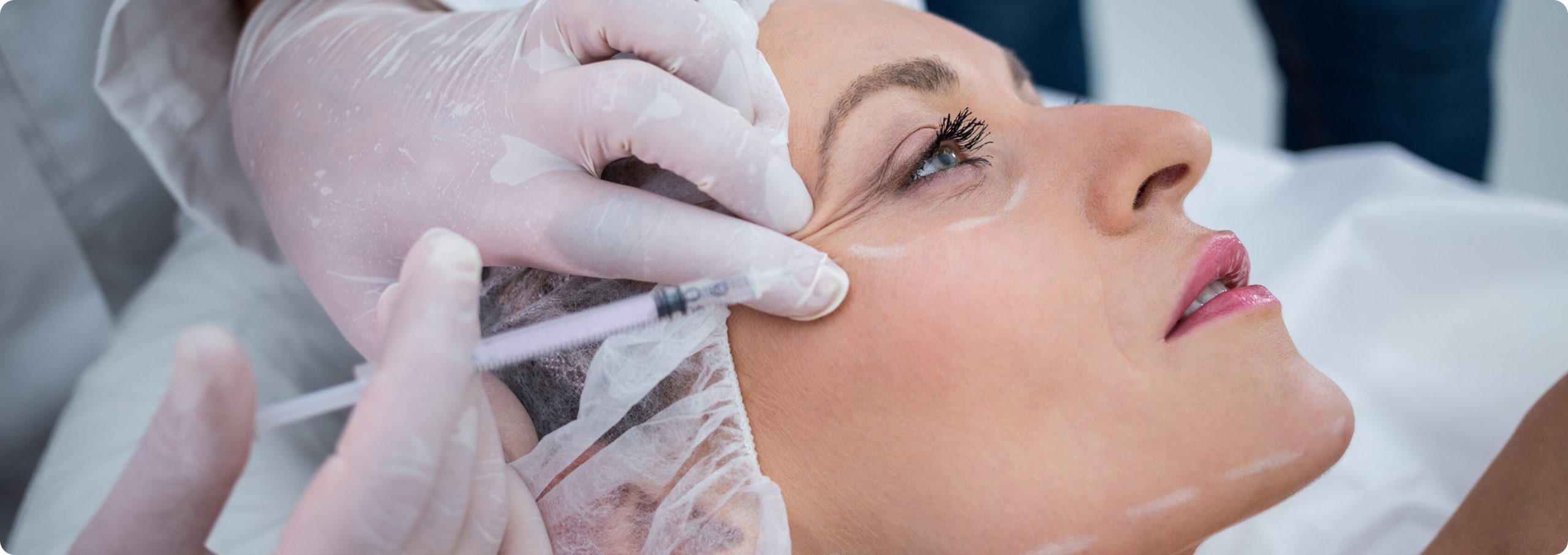 A close-up of a patient receiving a cosmetic injectable treatment from a medical professional wearing white gloves.
