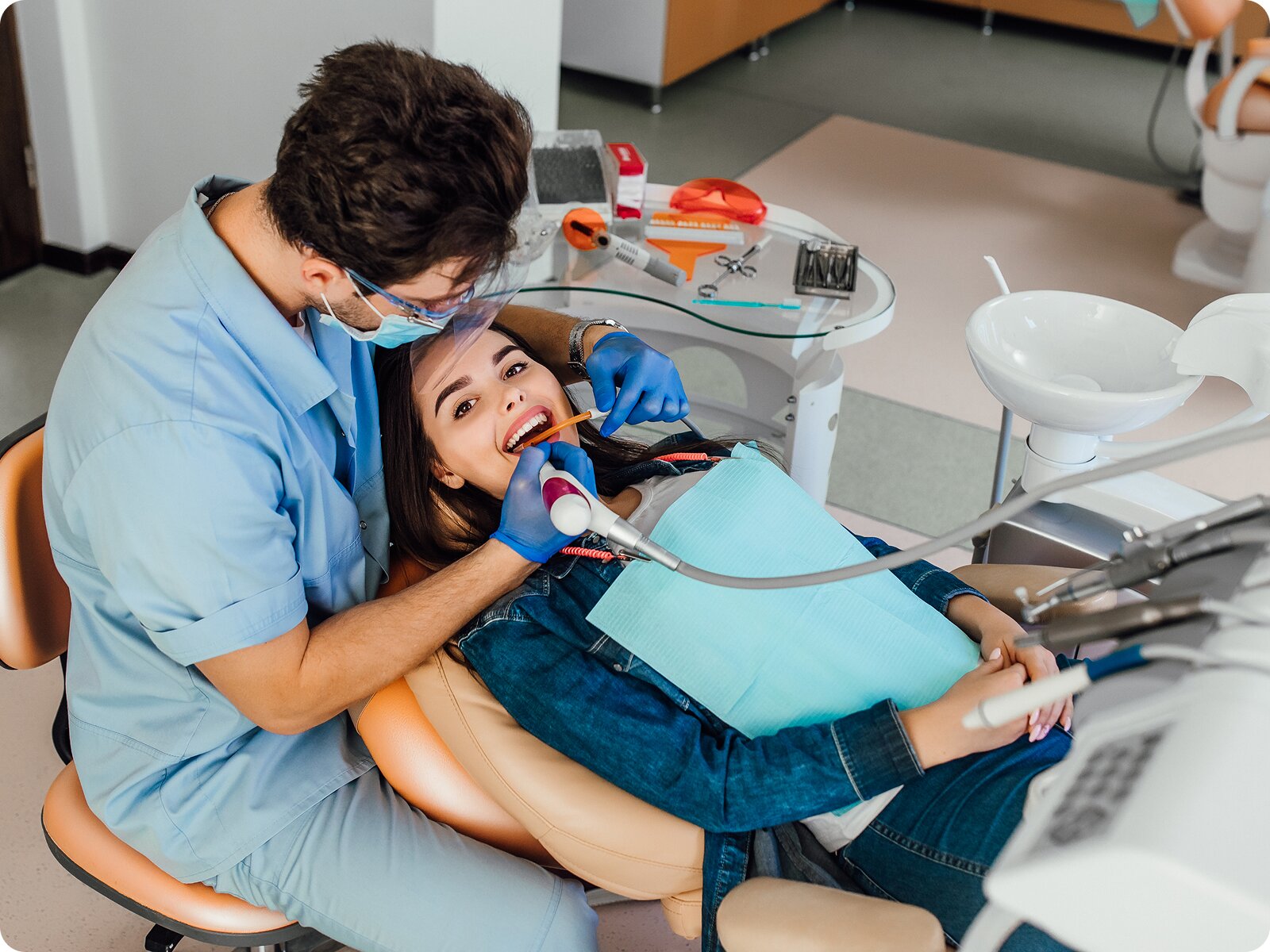 A male dentist treating a smiling female patient in a modern dental chair.
