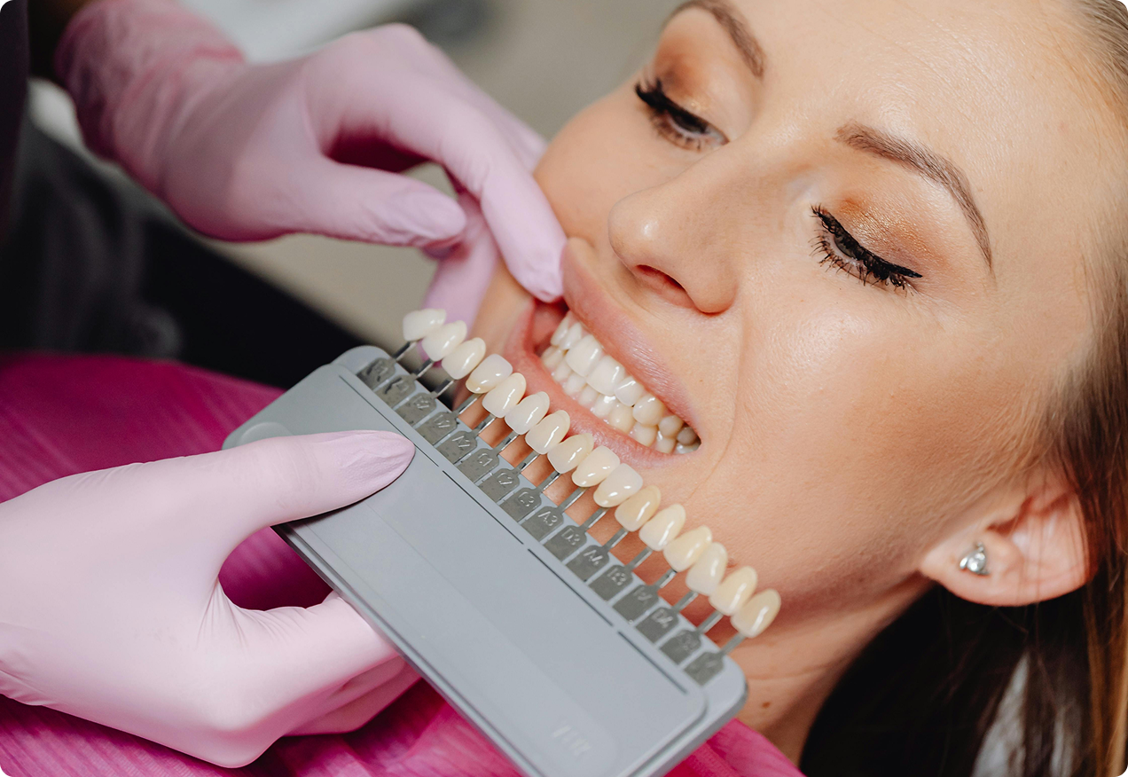 A dental professional in pink gloves using a shade guide to match the color of a patient's natural teeth.