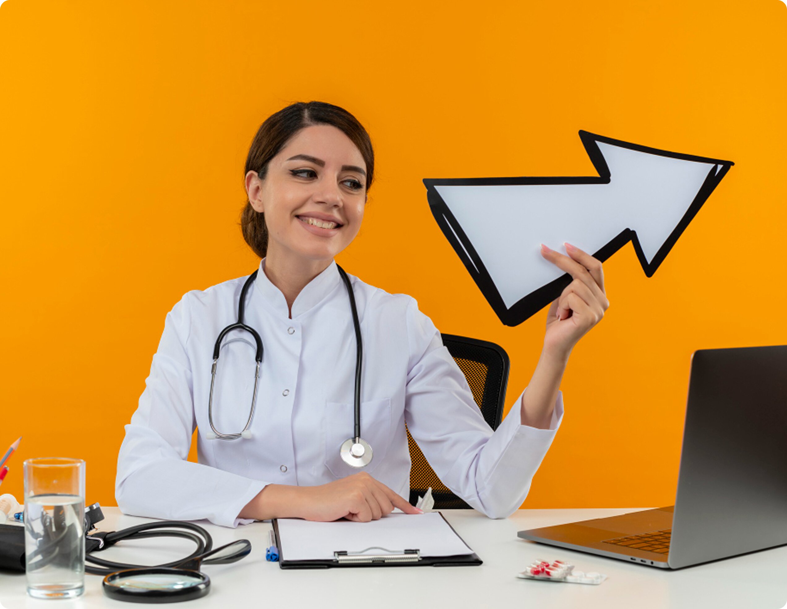 A female doctor in a white coat sitting at a desk with a laptop, smiling and holding a large white arrow pointing upward against a bright orange background.