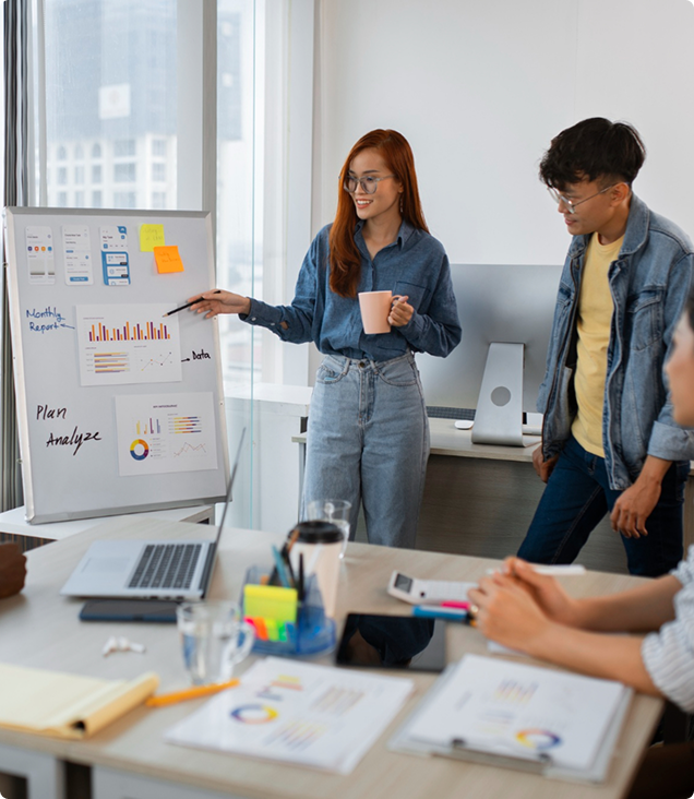 A marketing consultant presenting a monthly performance report and growth plan on a whiteboard to her team in a modern office.