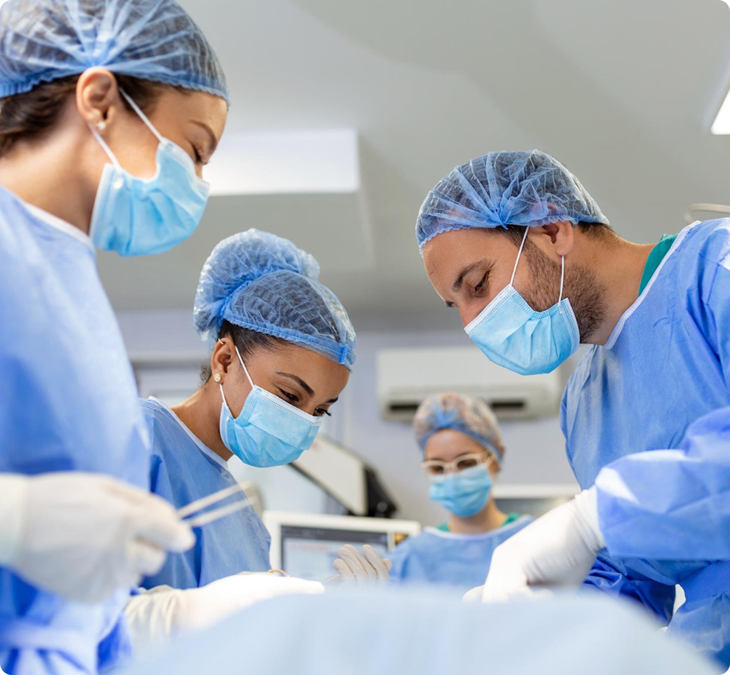 A team of cosmetic surgeons and medical staff in blue scrubs and surgical masks performing a procedure in a brightly lit operating room.