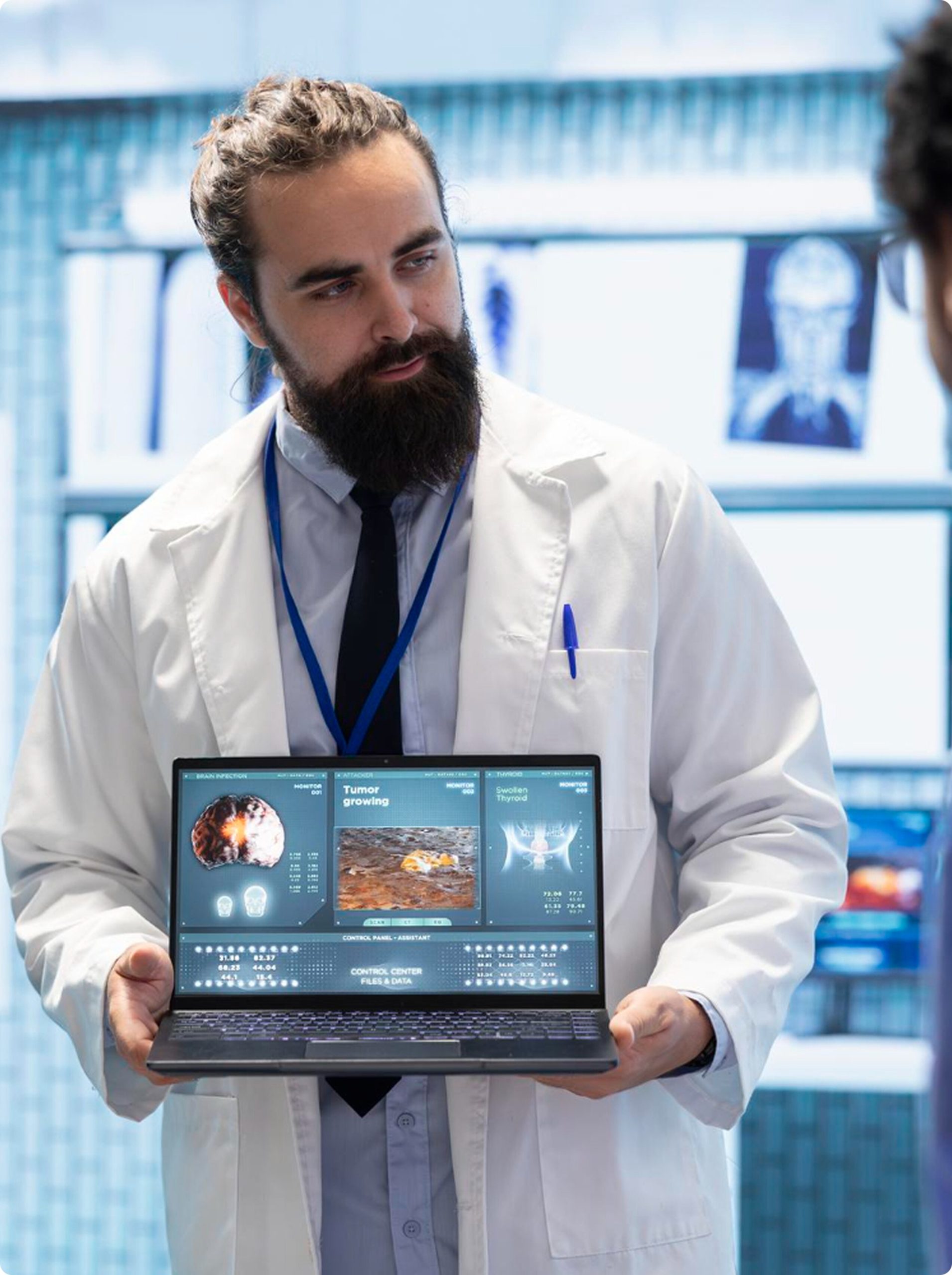 A male doctor in a white lab coat holding an open laptop displaying medical scans and digital healthcare data.
